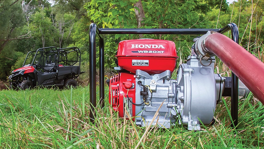 Close up of pump in foreground with side-by-side and man using hose in background