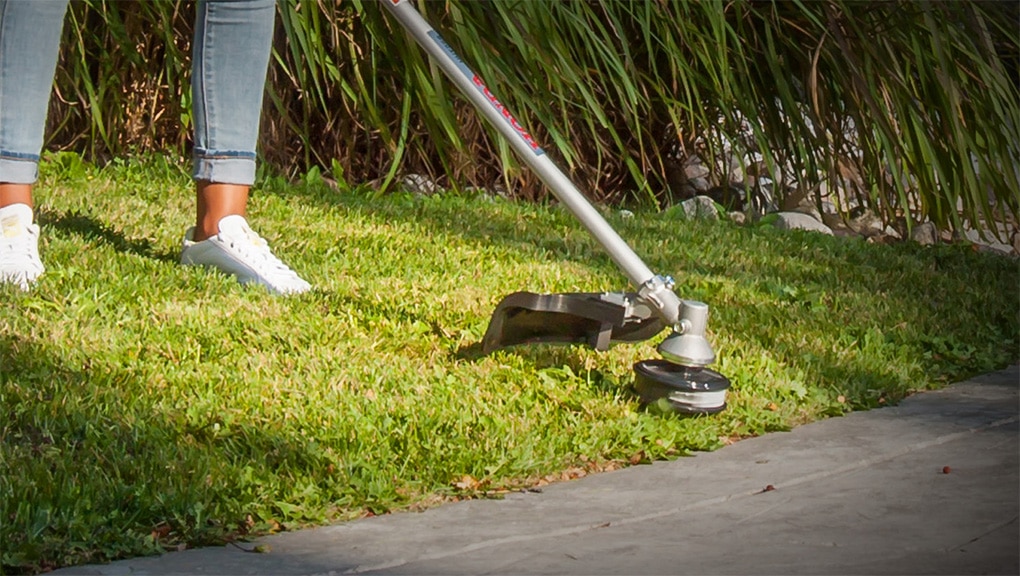 Close up of woman using trimmer on grass along driveway